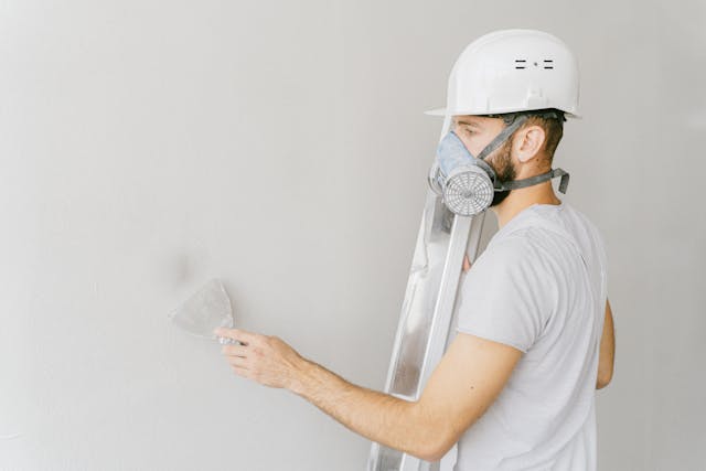 man-in-mask-using-flat-metal-spatula-on-the-wall